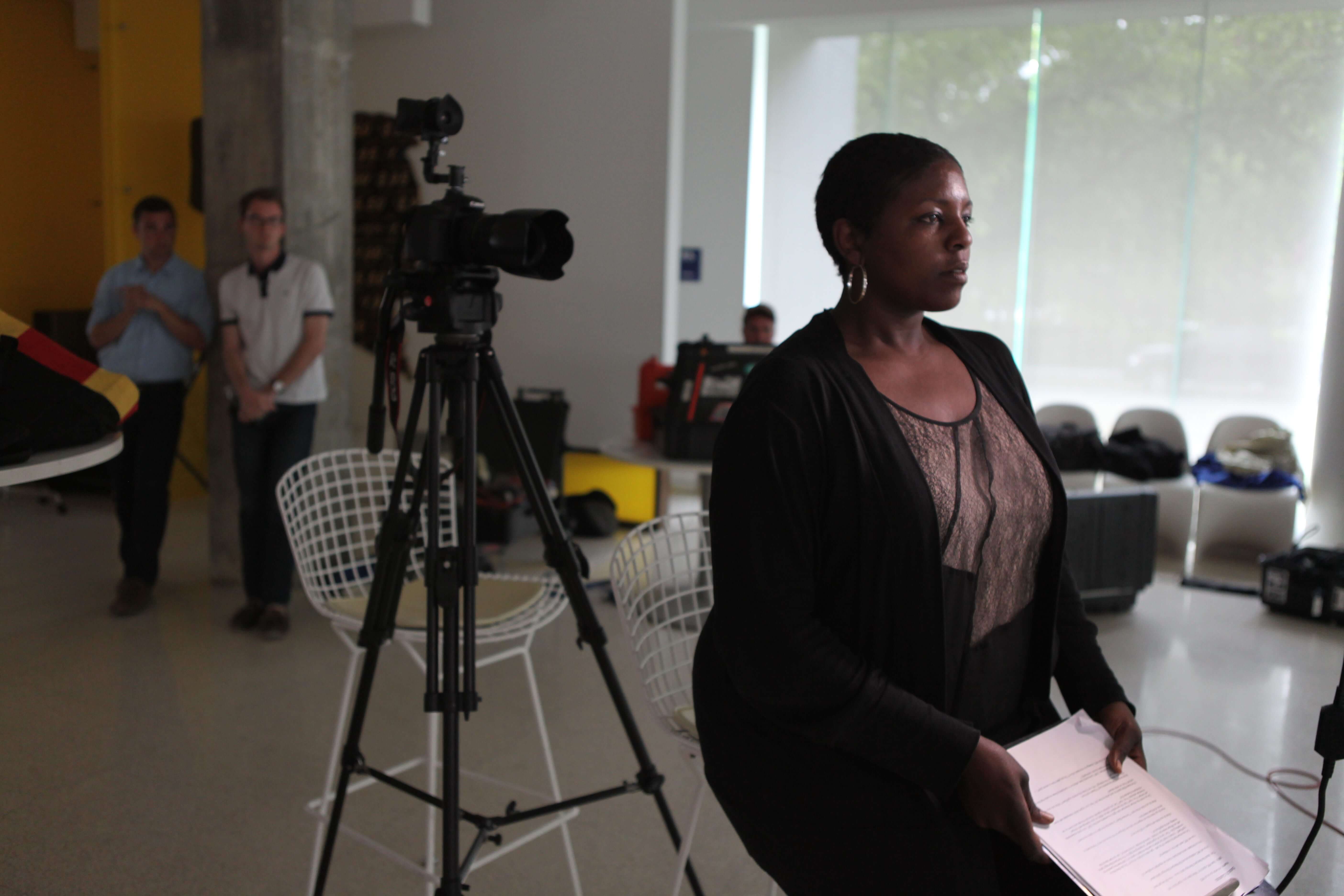 A woman standing in front of a camera looks at her notes