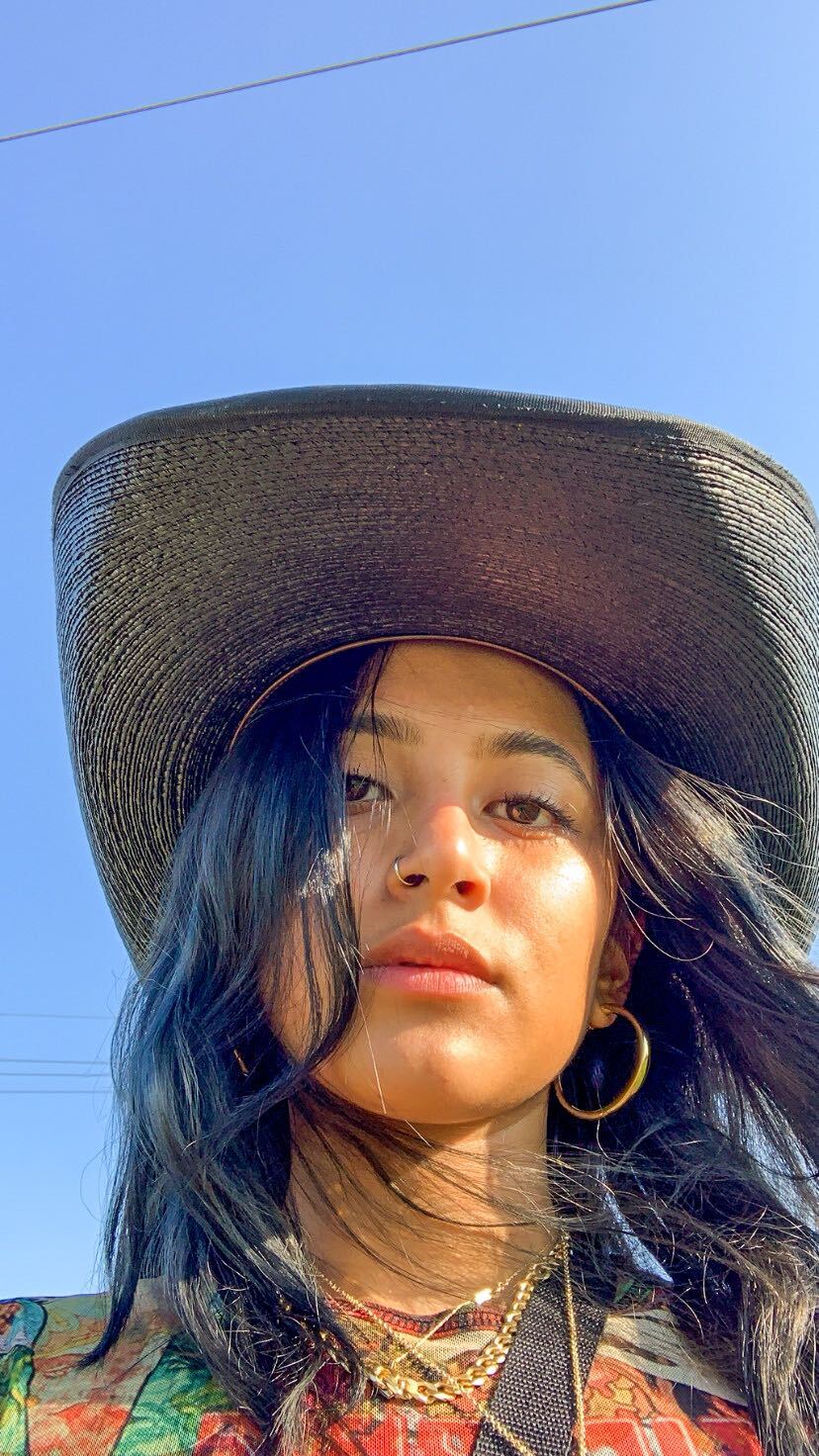 Leslie is wearing a cowboy hat and hoop earrings. The sky is in the background.