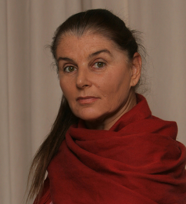 A portrait of a woman in a red draping top looking into the camera.