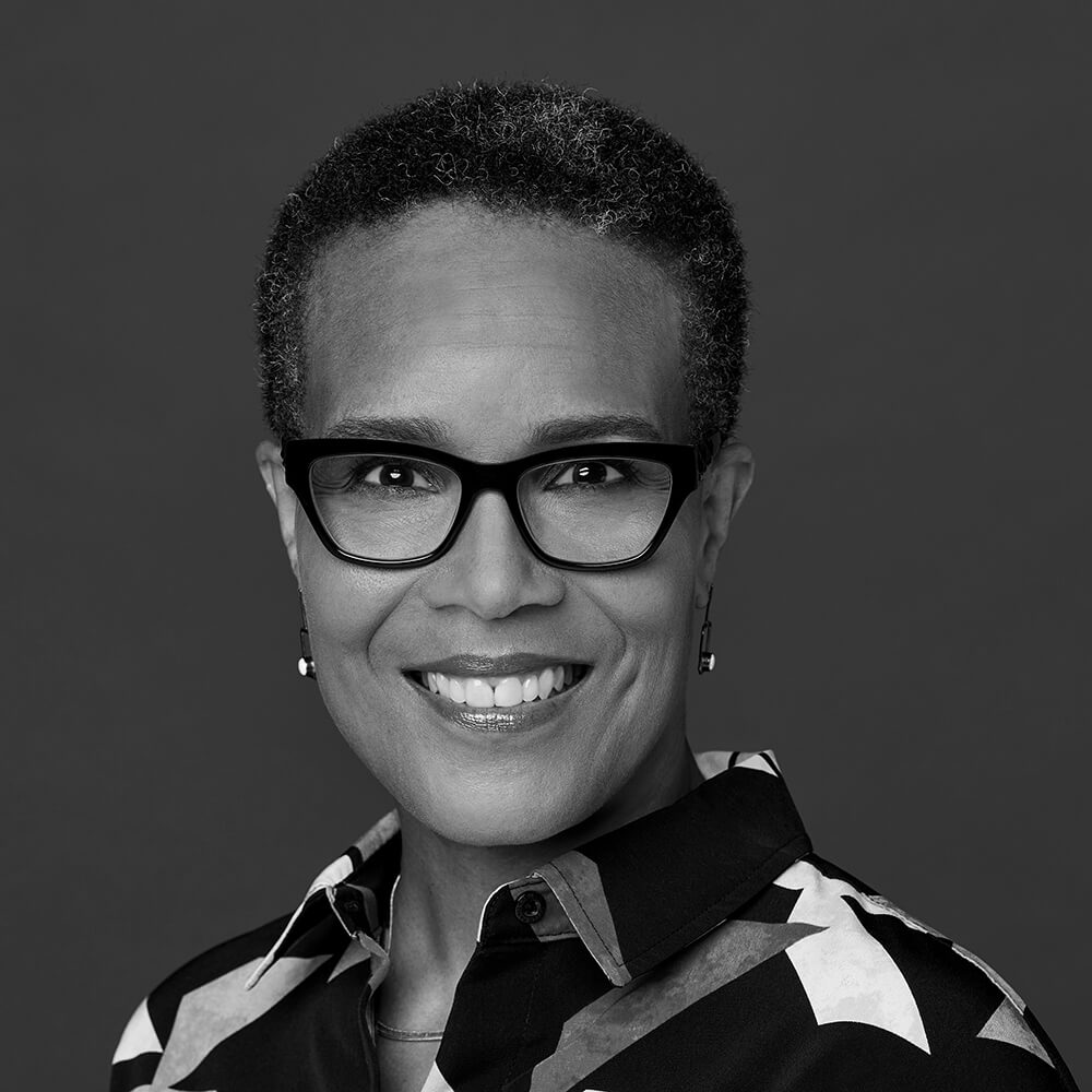 Tracy Heather Strain smiles wearing black glasses and a geometric-patterned blouse.