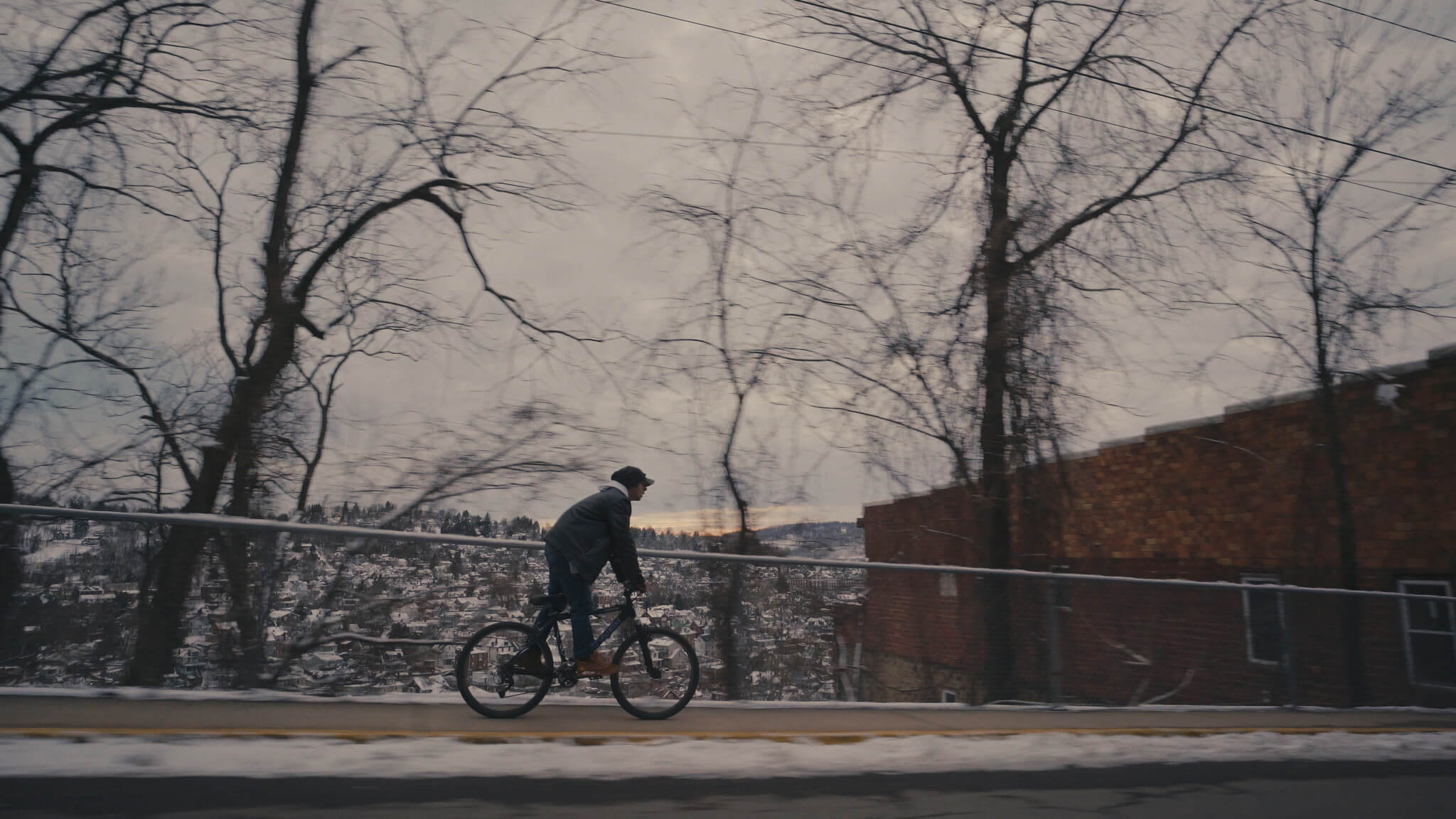 Still from Recovery Boys. Ryan rides his bike to work in a wintry Morgantown, West Virginia.