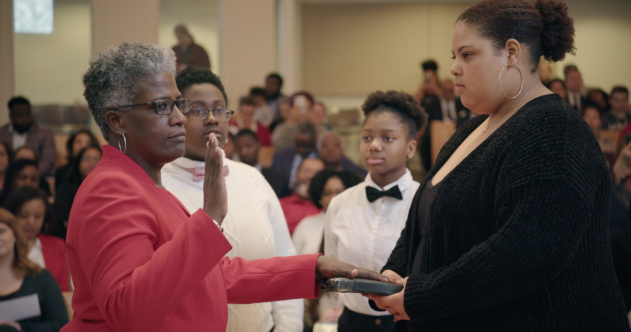 Still from I am not going to change 400 years in four. A woman places her hand on a bible and swears in.