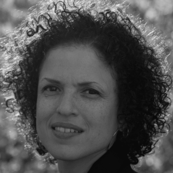 Headshot of a woman with short curly hair, looking at the camera and with a blurry background