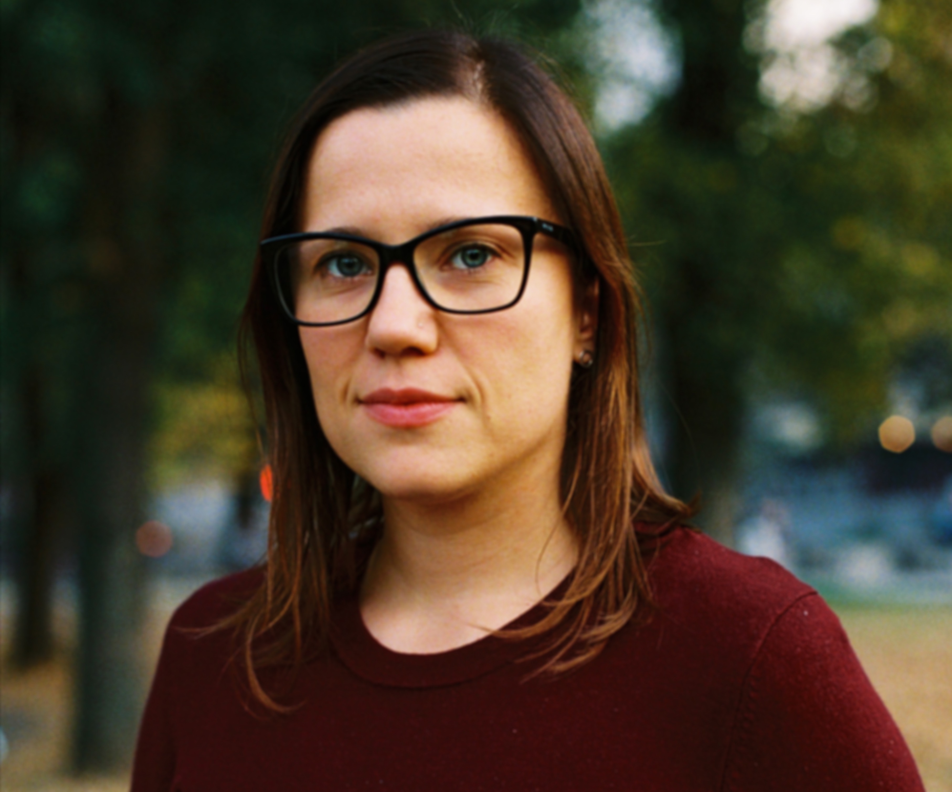 Marija Stojnic, a woman wearing black glasses and a burgundy shirt, looks directly at the camera and smiles. 