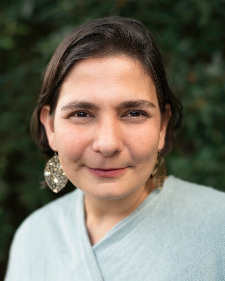 Eliza Licht looking directly at camera. She is wearing earrings and is in front of an out focus background. 