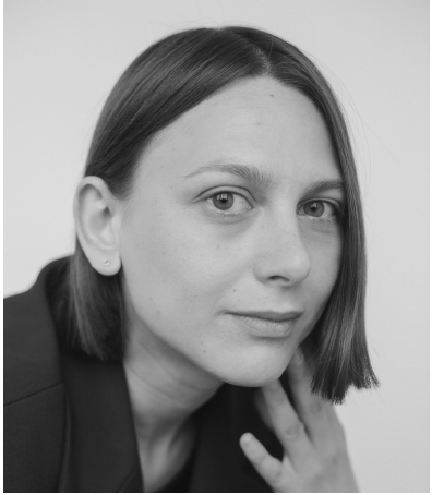 Oksana Karpovych looking directly at the camera. She has short brown hair and has her hand close to her face. Black and white portrait. 