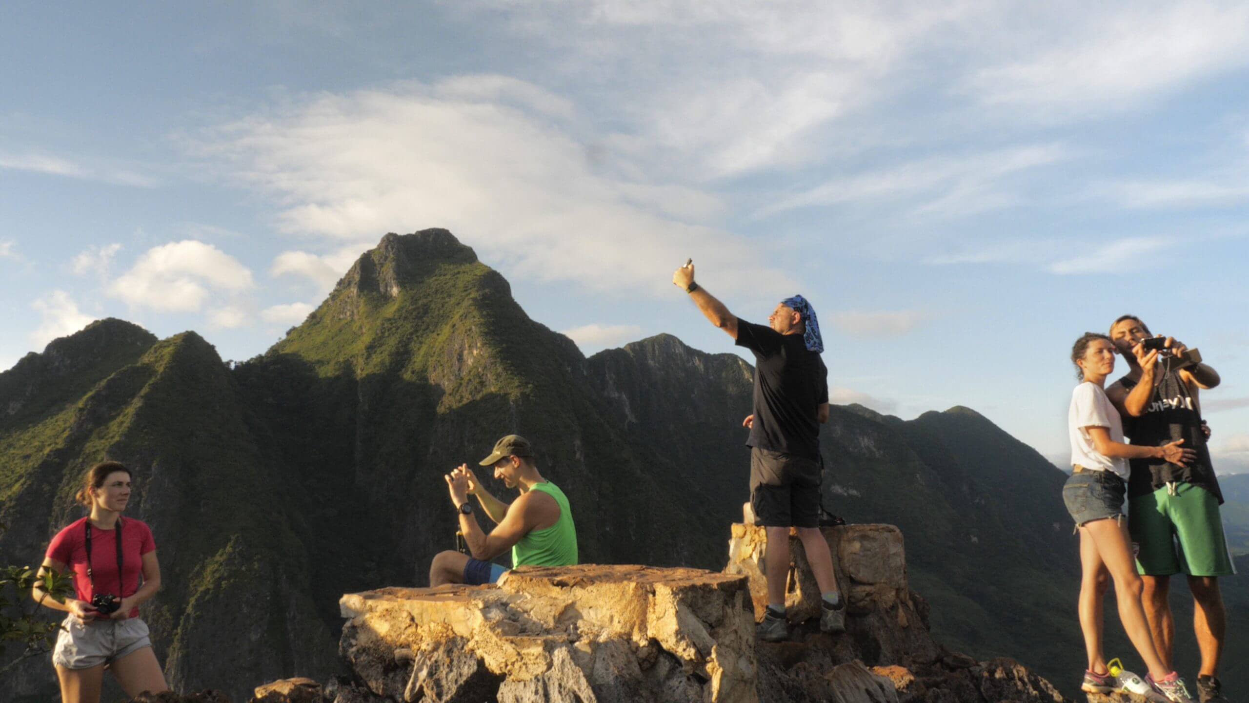 Still from Onlookers. Tourists stand on a mountaintop in Laos taking photos and selfies.