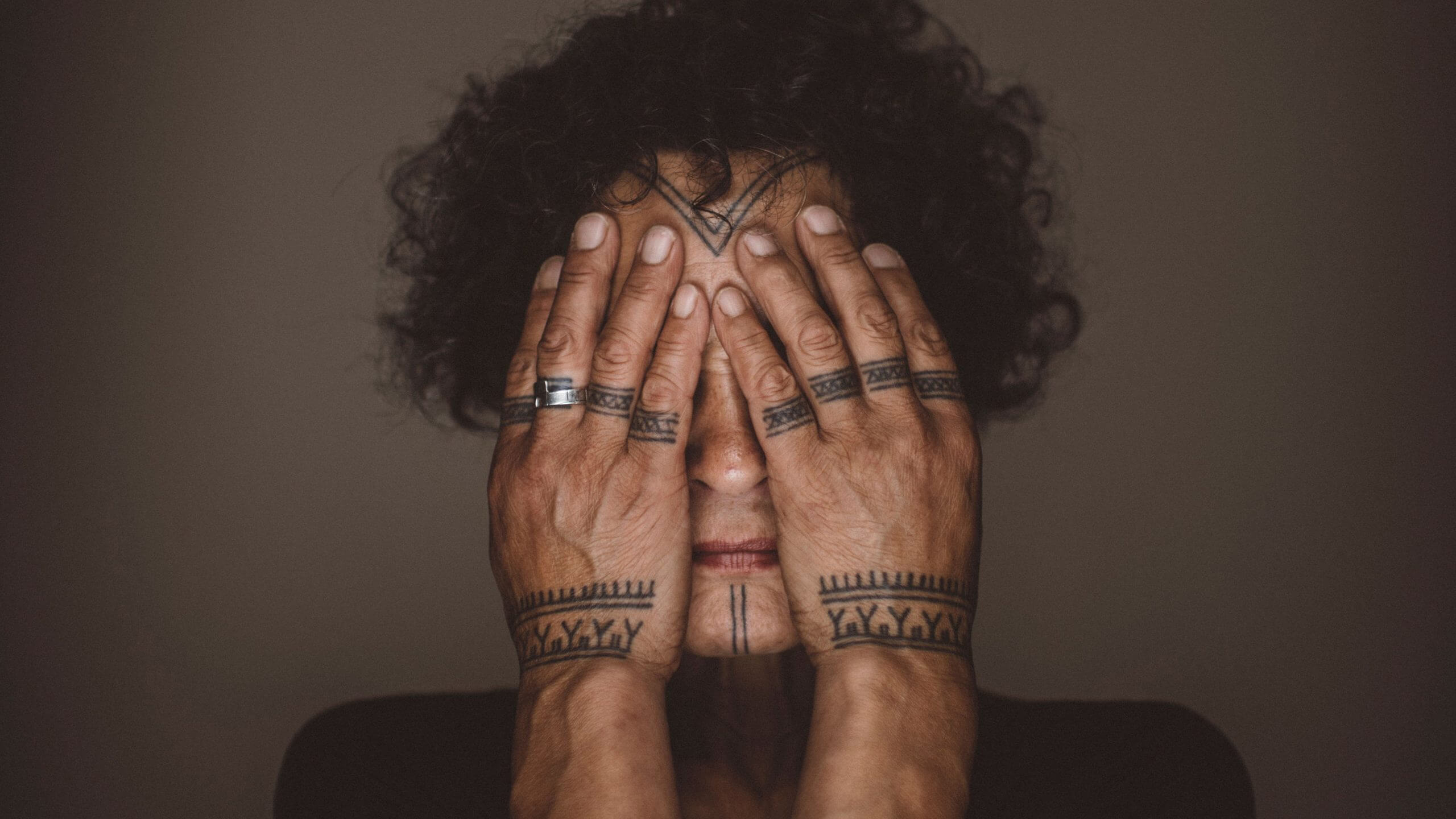 The main character of Twice Colonized, Aaju Peter, in a close-up shot holding her hands in front of her face so her traditional tattoos on her hands and her chin are visible.