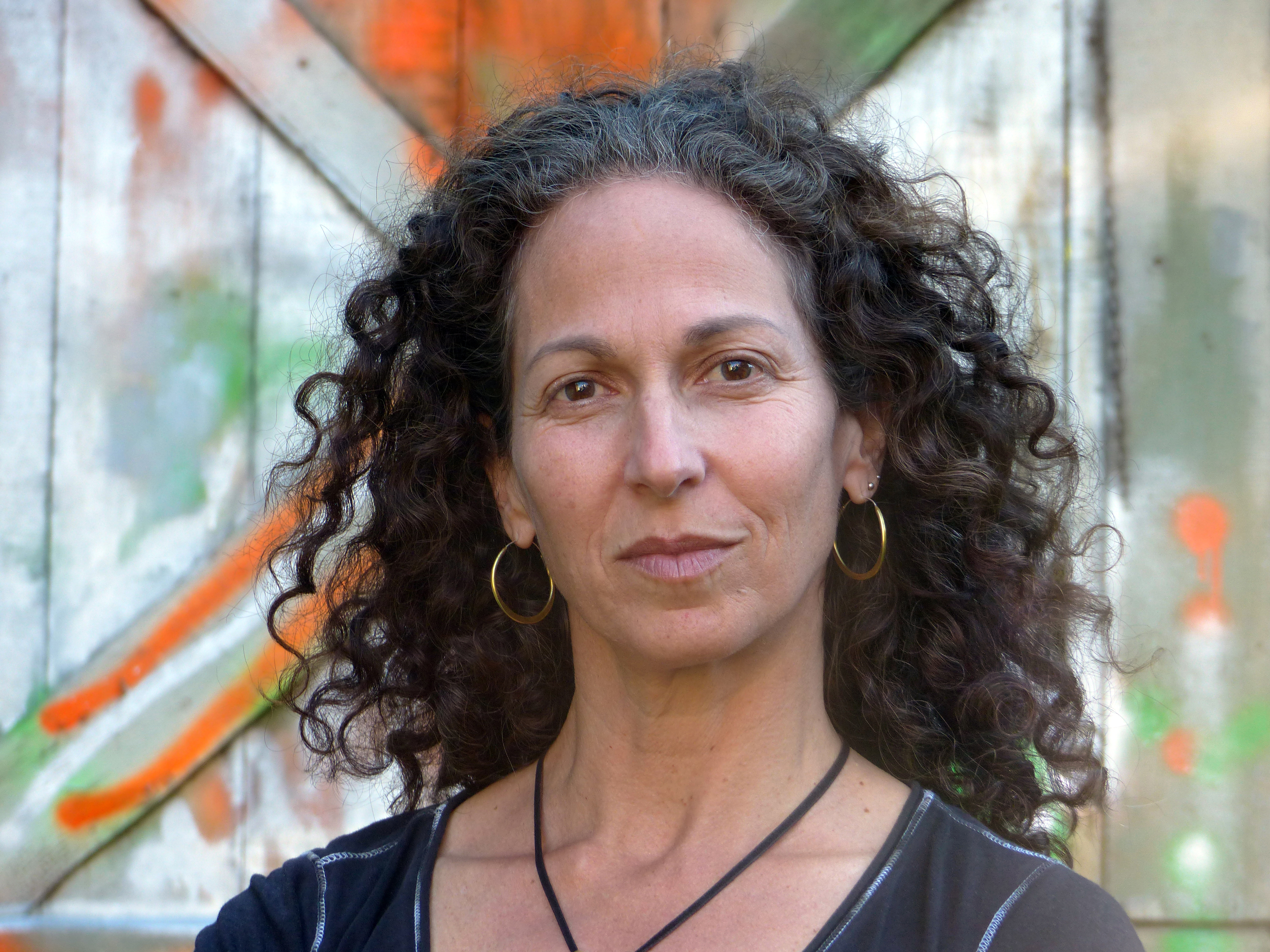 Jane Greenburg looking directly at the camera. She wears a beanie standing in front of a wooden door.