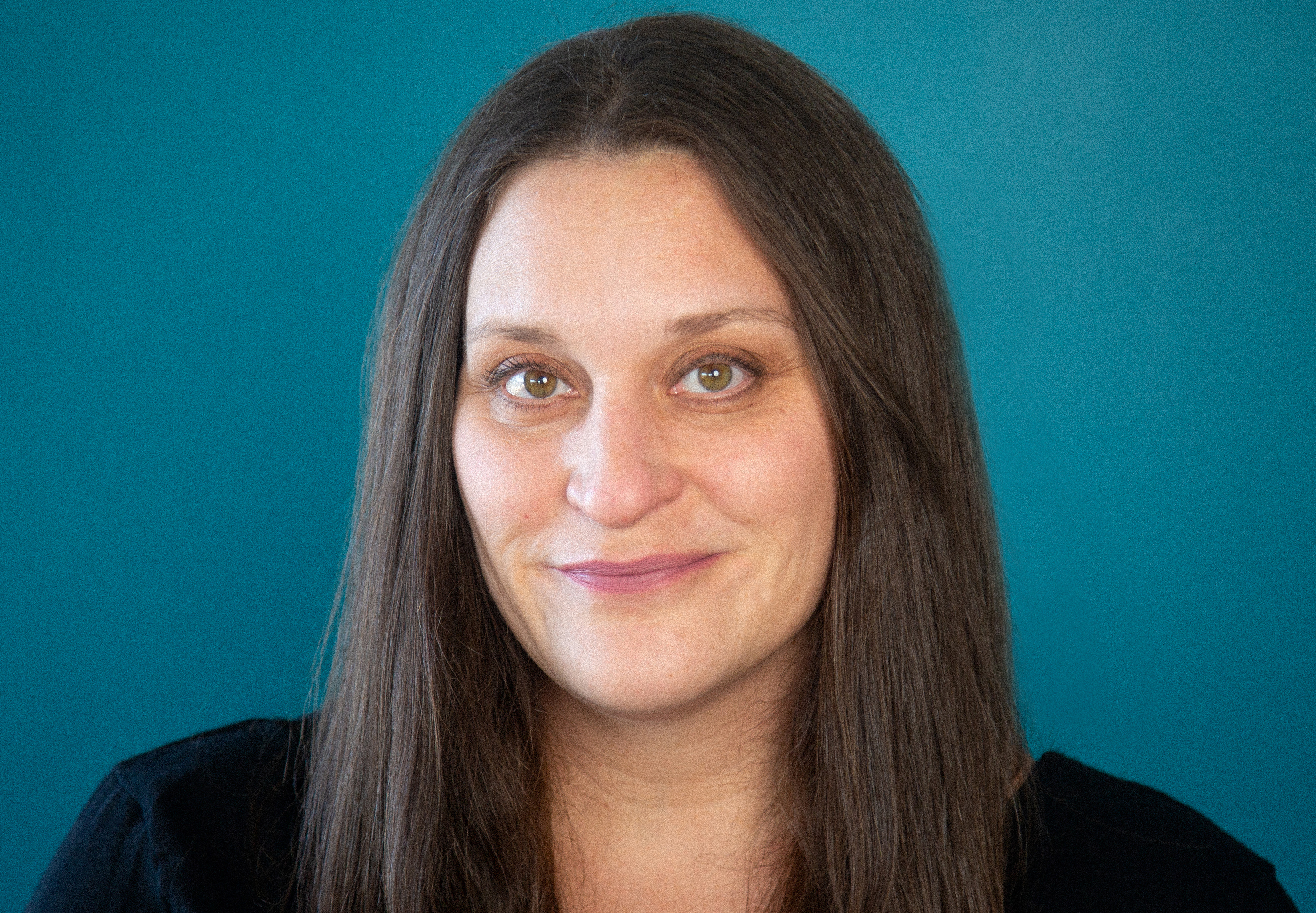 Headshot of Margaret Byrne. A woman looking at the camera with long hair parted in the middle and slightly smiling at the camera.