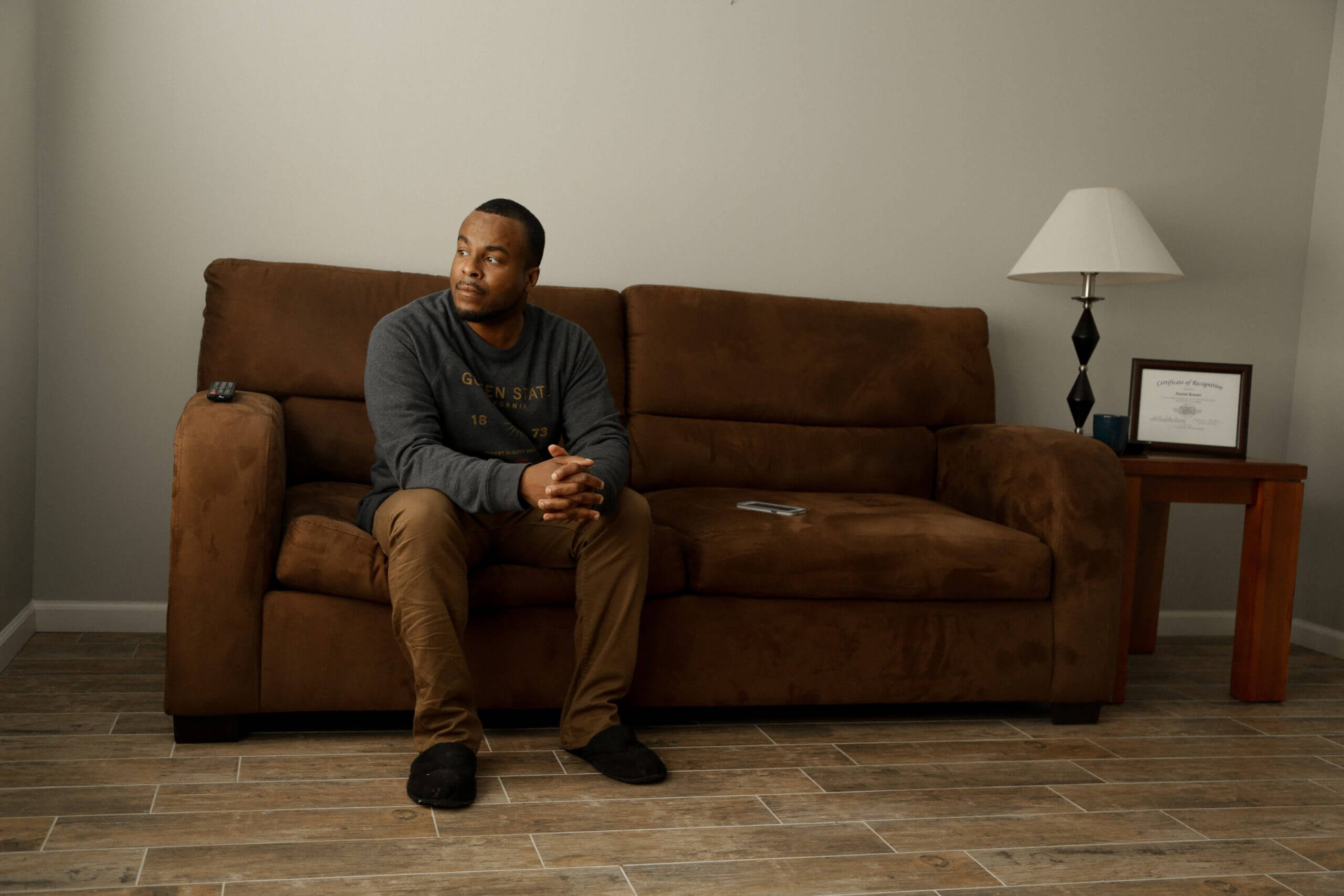 A man sits on a couch with his arms in front of him looking out a nearby window.