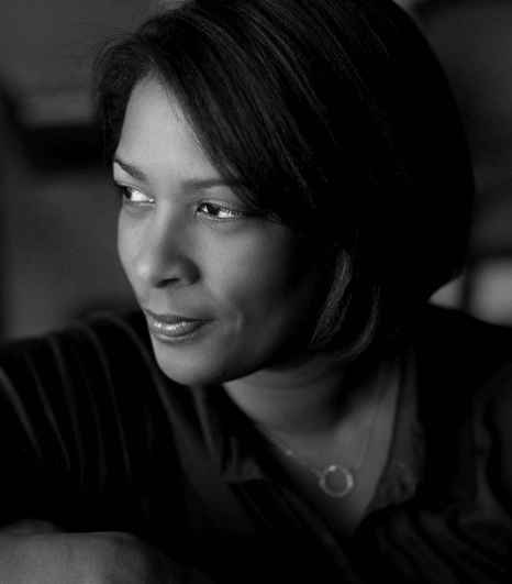 Dawn Porter has short hair, wears a necklace, and a long sleeve v-neck blouse. She smiles with her face looking towards the side. Black and white portrait.