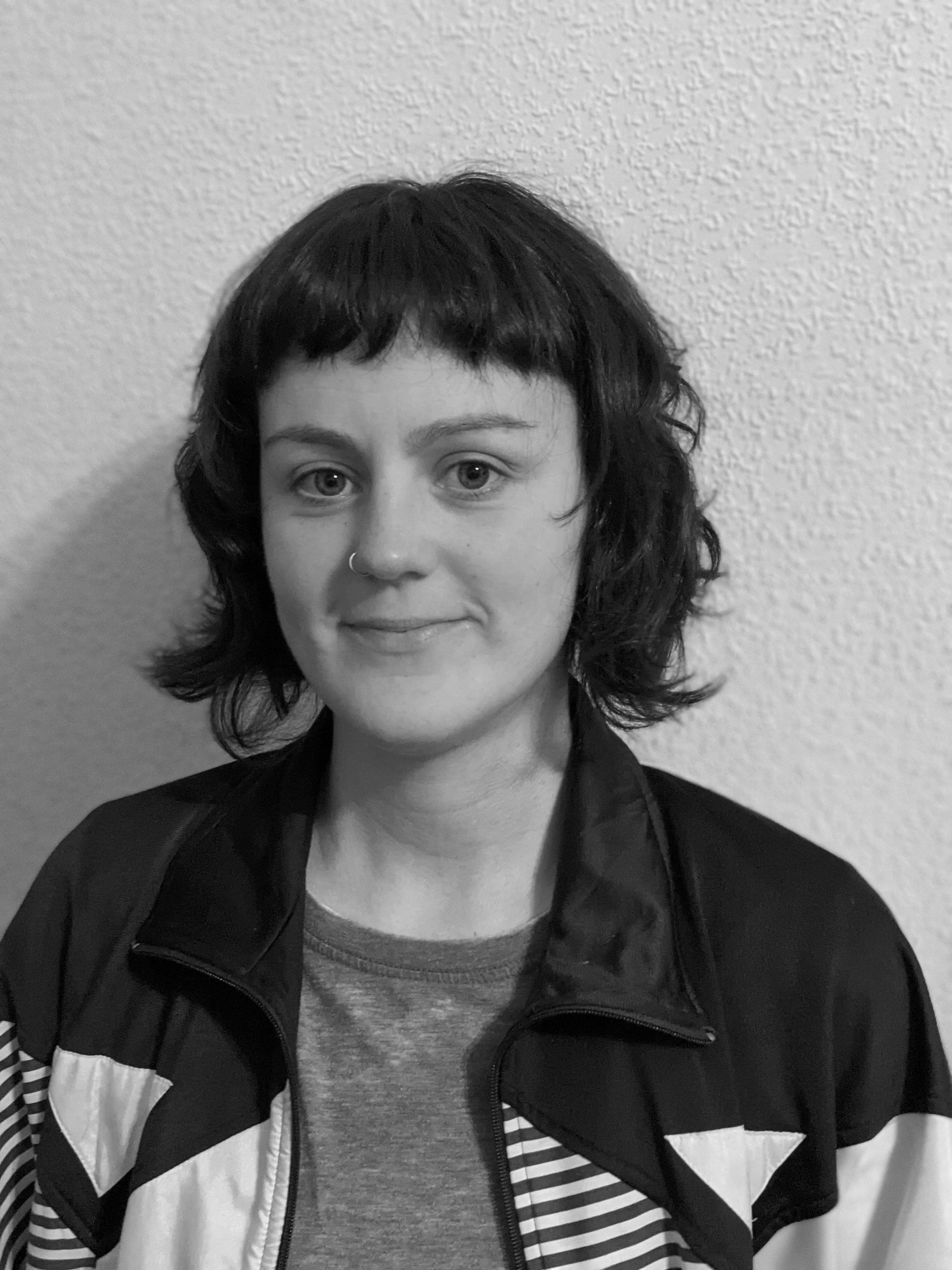 A black and white portrait of a young woman with bangs and a short haircut against a light wall.