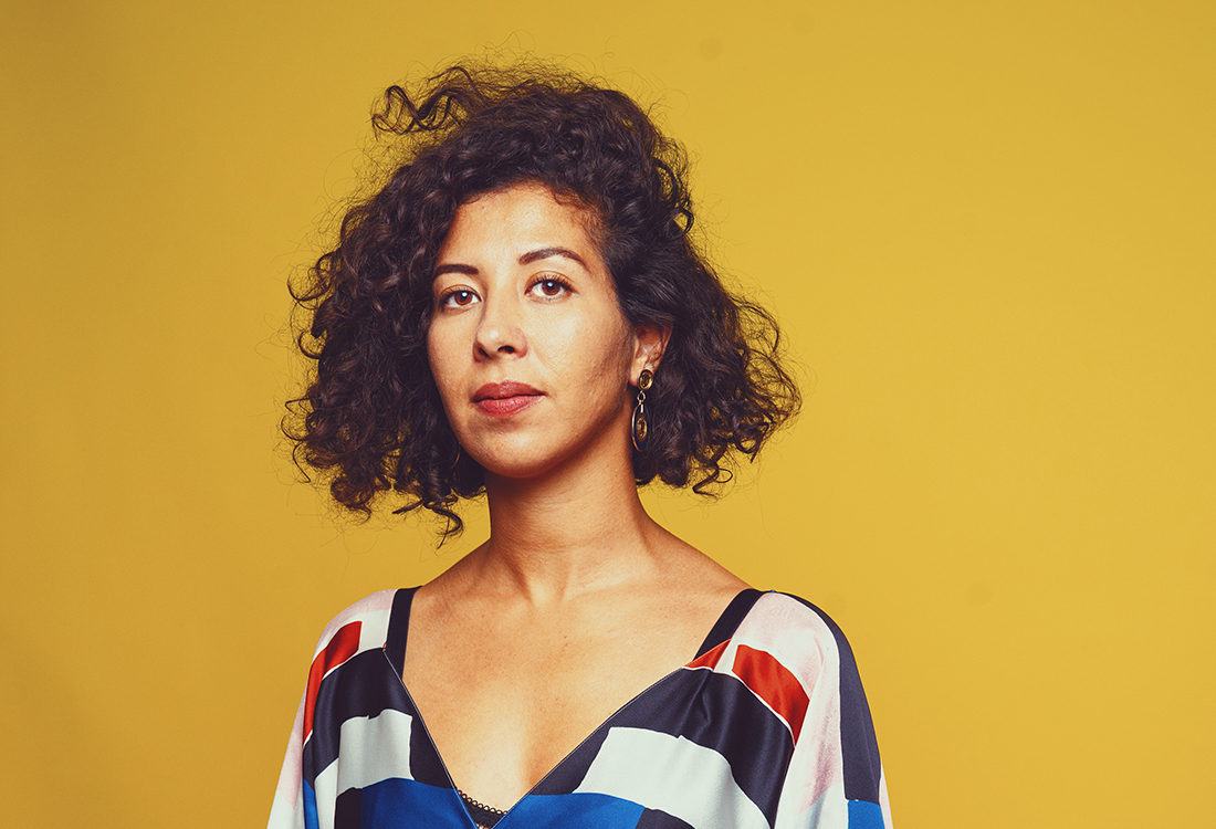 Assia Boundaoui with short curly hair against a yellow background