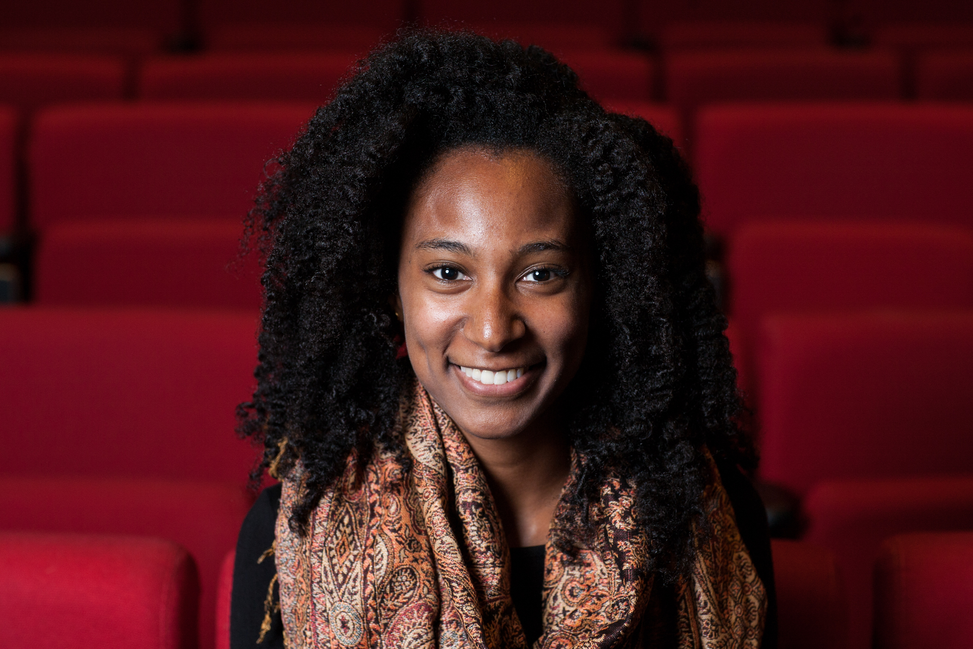 Chelsi Bullard looking directly ahead and smiling. She has very curly, shoulder-length hair and wears a patterned scarf. 