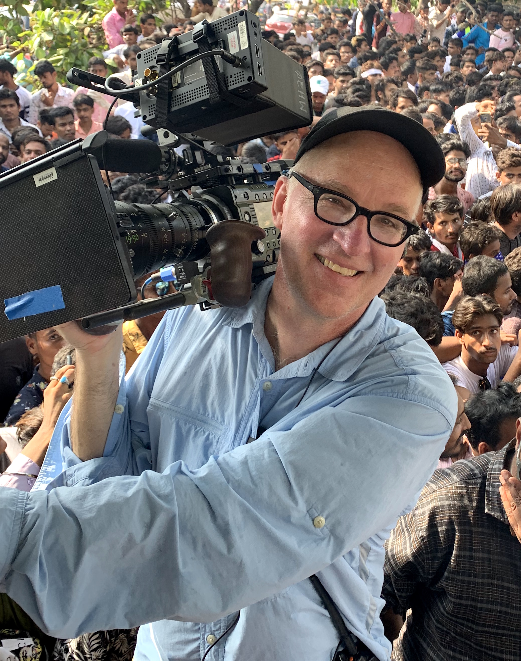 Jerry Risius holds a camera on his shoulder and smiles directly at the camera.