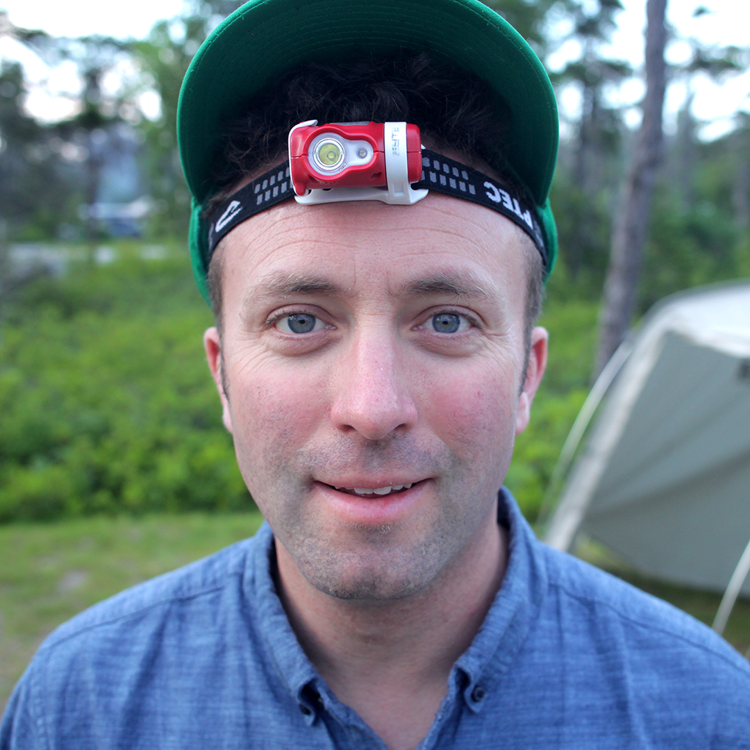 Headshot of Ian Cheney from the shoulders up wearing a headlight and button down collared shirt