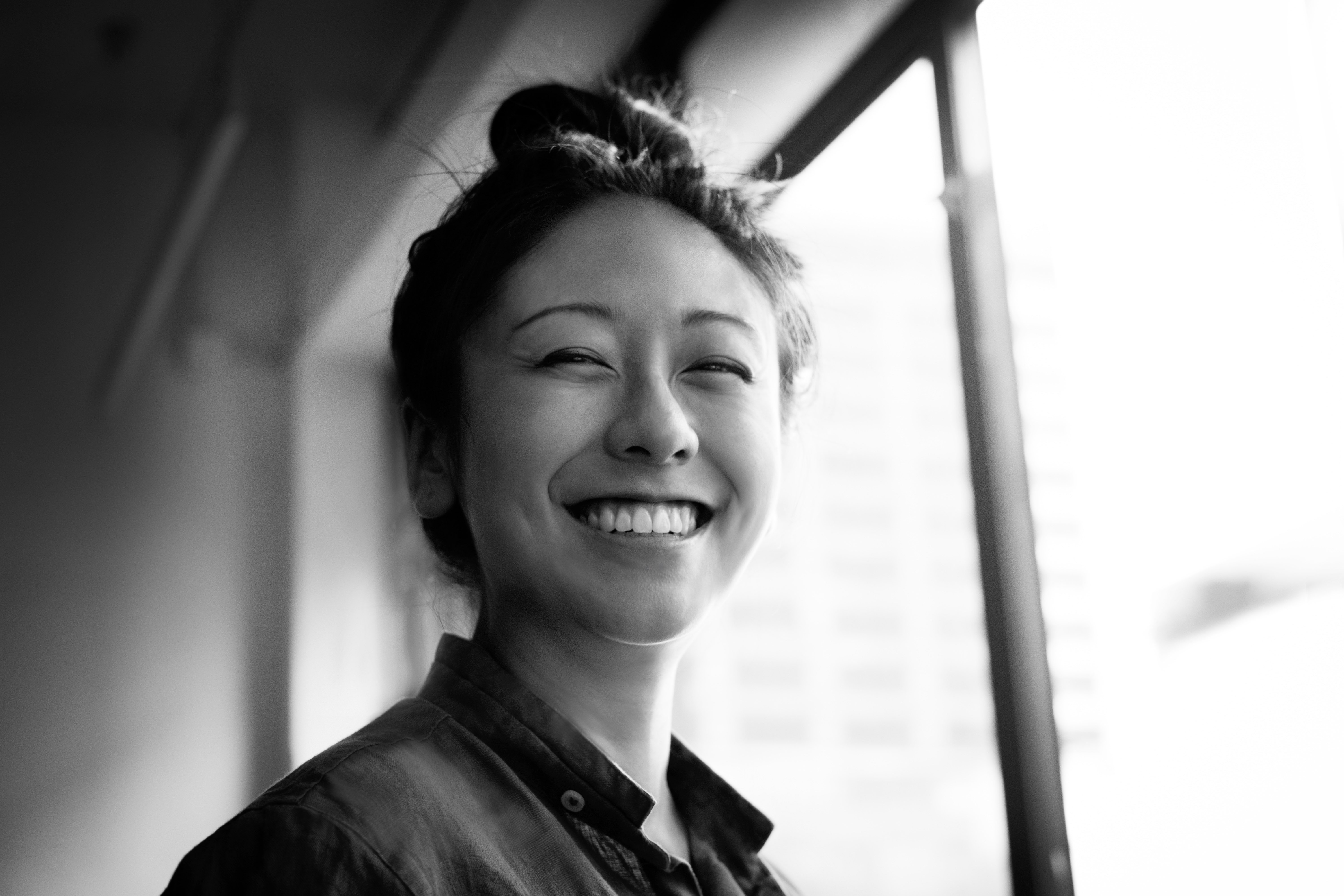 Portrait of a woman with a top knot bun, smiling widely at the camera