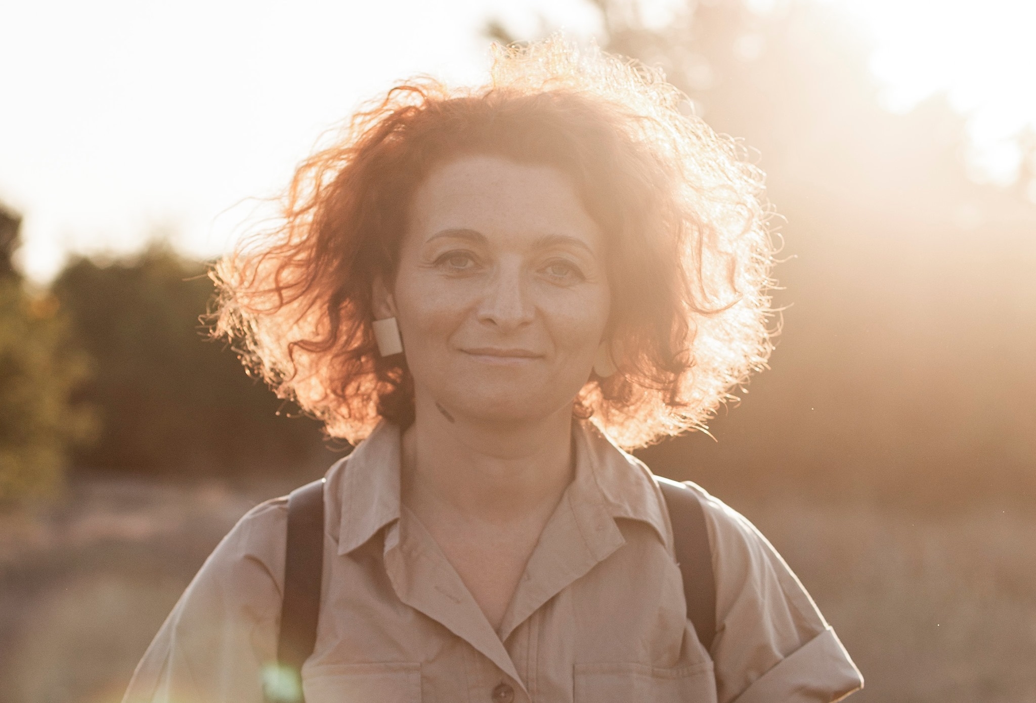 Portrait of a woman facing the camera, she wears a short sleeve shirt, and has medium wavy hair, there is a flare on the upper right side corner