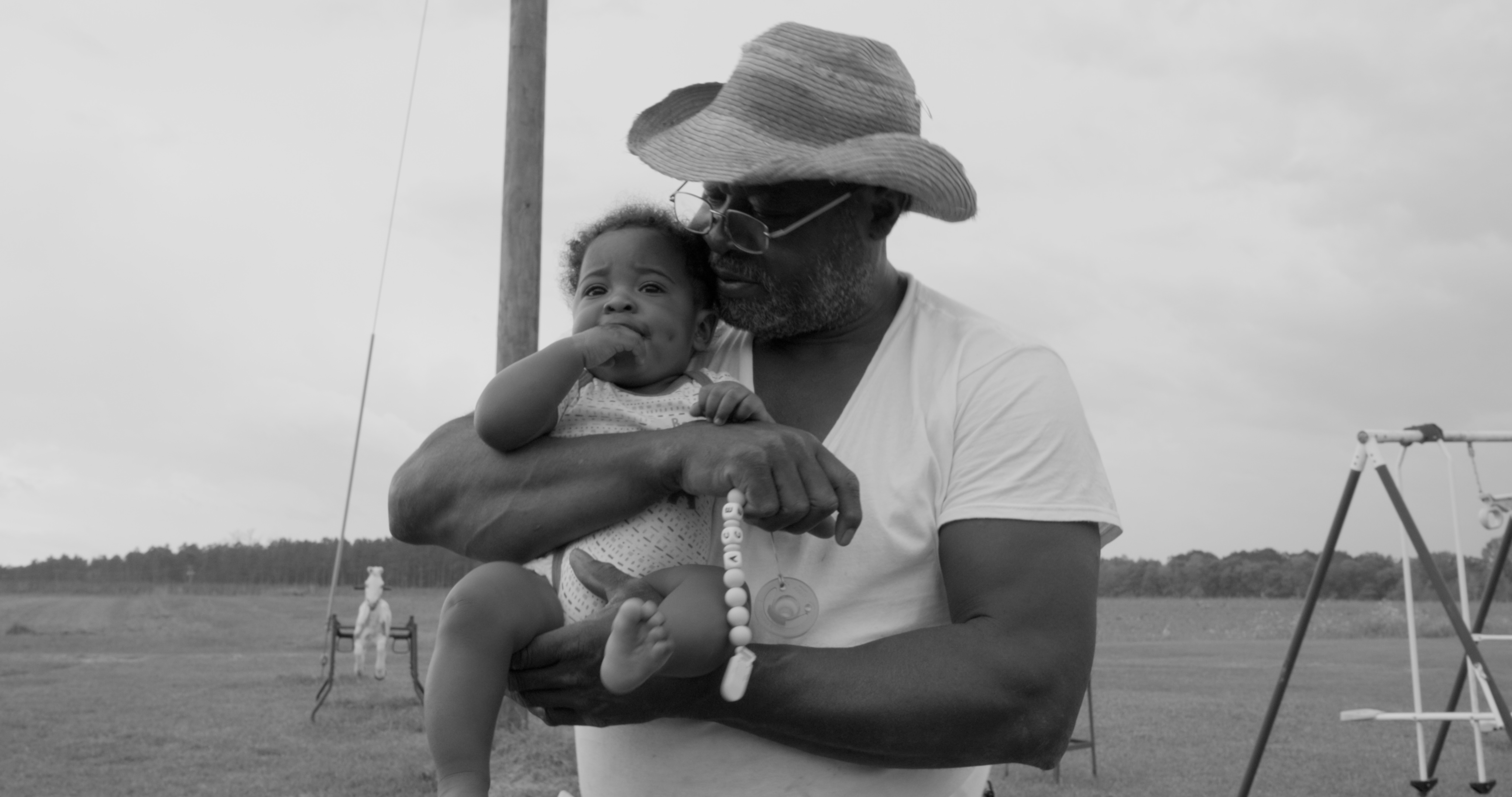 Still from Seeds. A man holds a young baby on a boat. Photo in black and white.