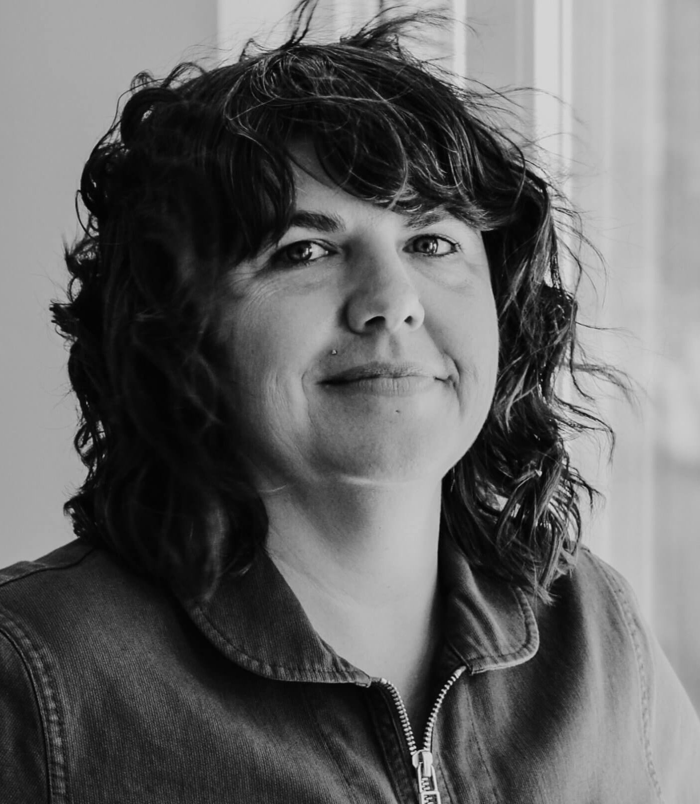 Portrait of Jess Devaney smiling at the camera in black and white.