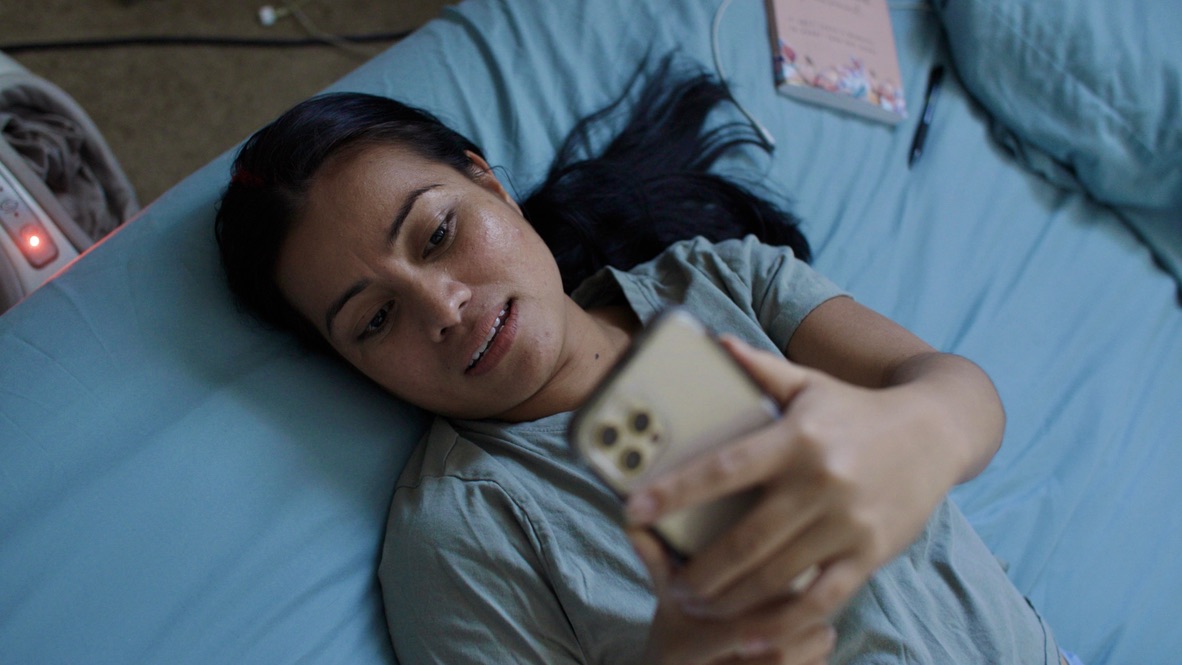 A still from Dear You. Grace Jones lay on her bed while looking up at her phone.