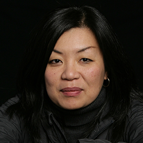 Headshot of a woman with dark hair and hoops smiling slightly at the camera