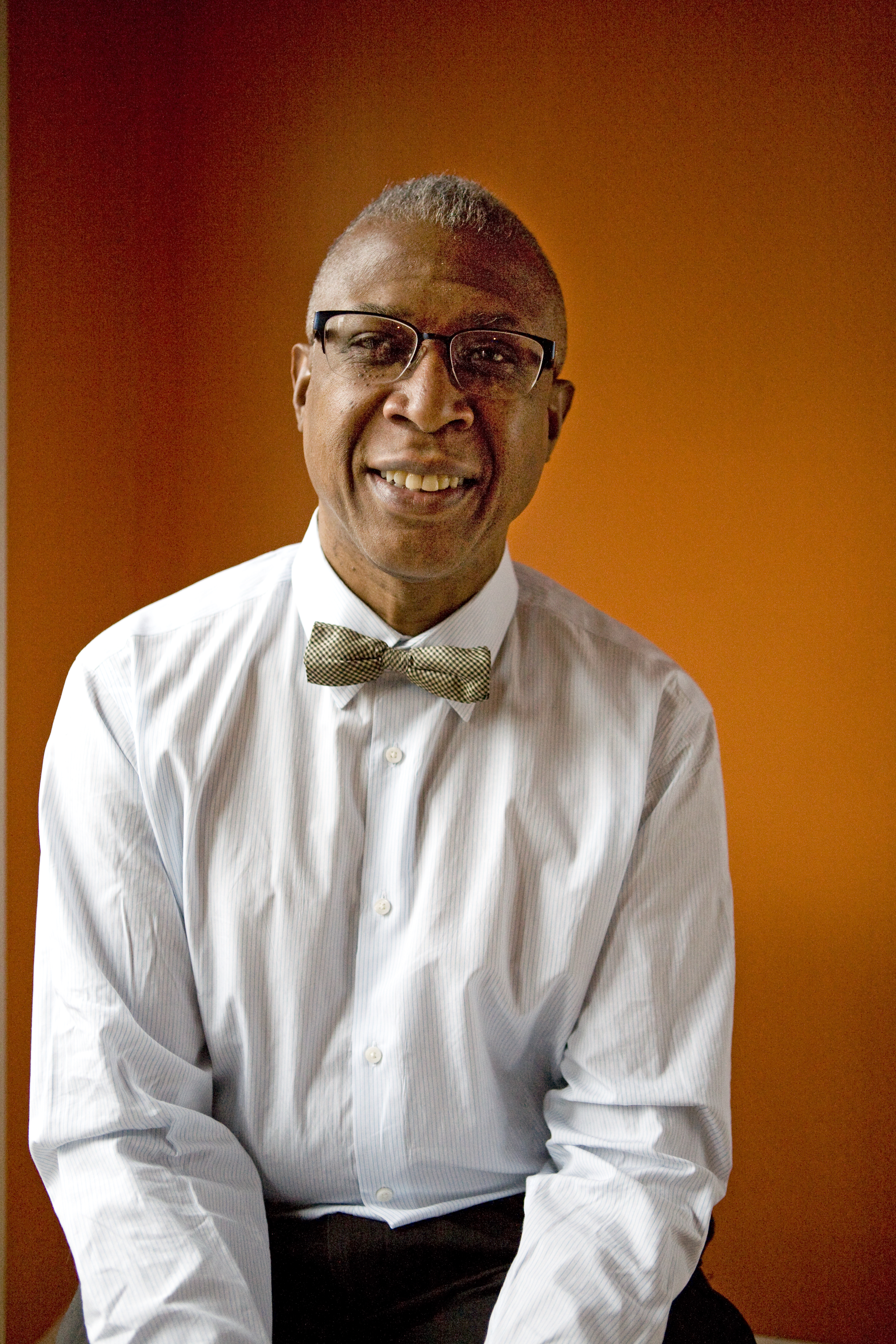 A portrait of a man wearing a bowtie in front of an orange backdrop.