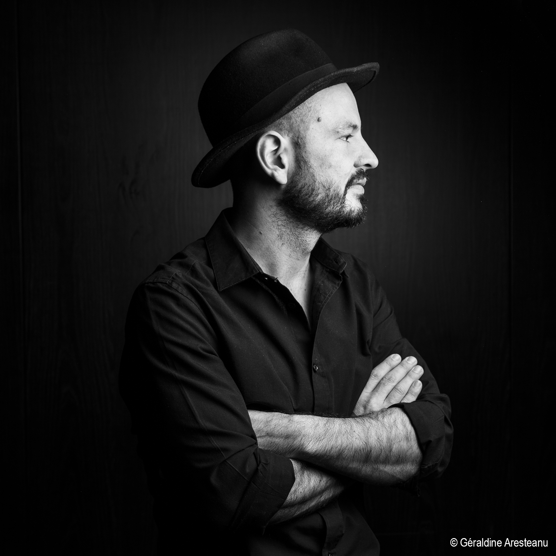 Profile shot of a man with beard and a fedora hat, wearing a shirt