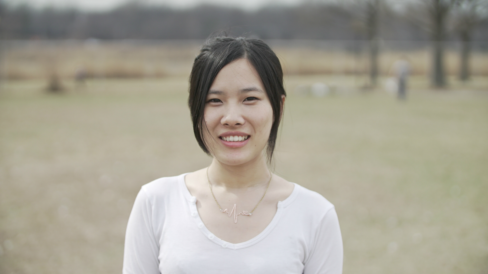 Headshot of Siyi Chen from the chest up wearing a white shirt outside in a field