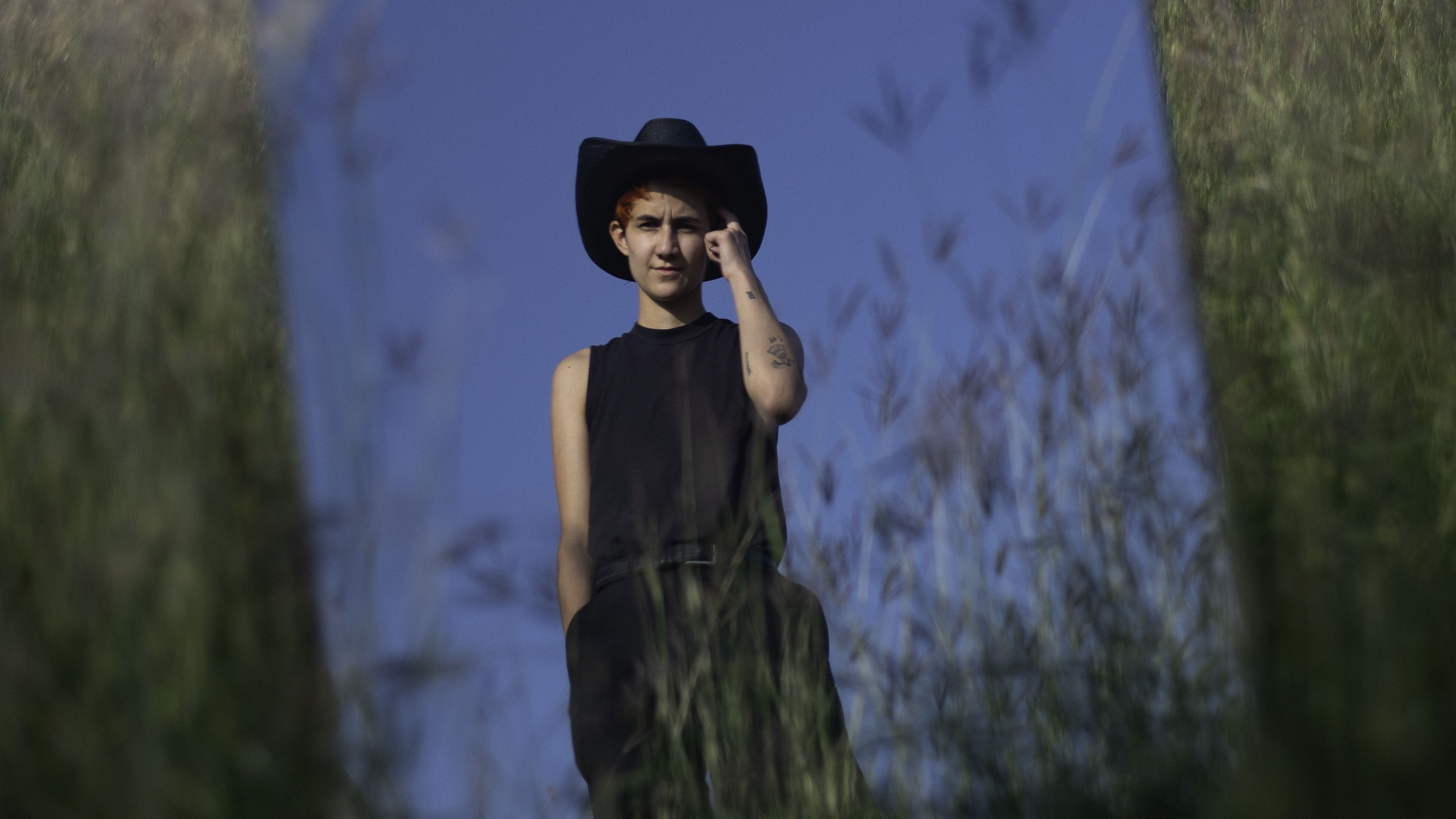 Portrait of Ana Rodriguez, wearing a sleeveless shirt, cowboy hat and touching the left side of her head with a finger