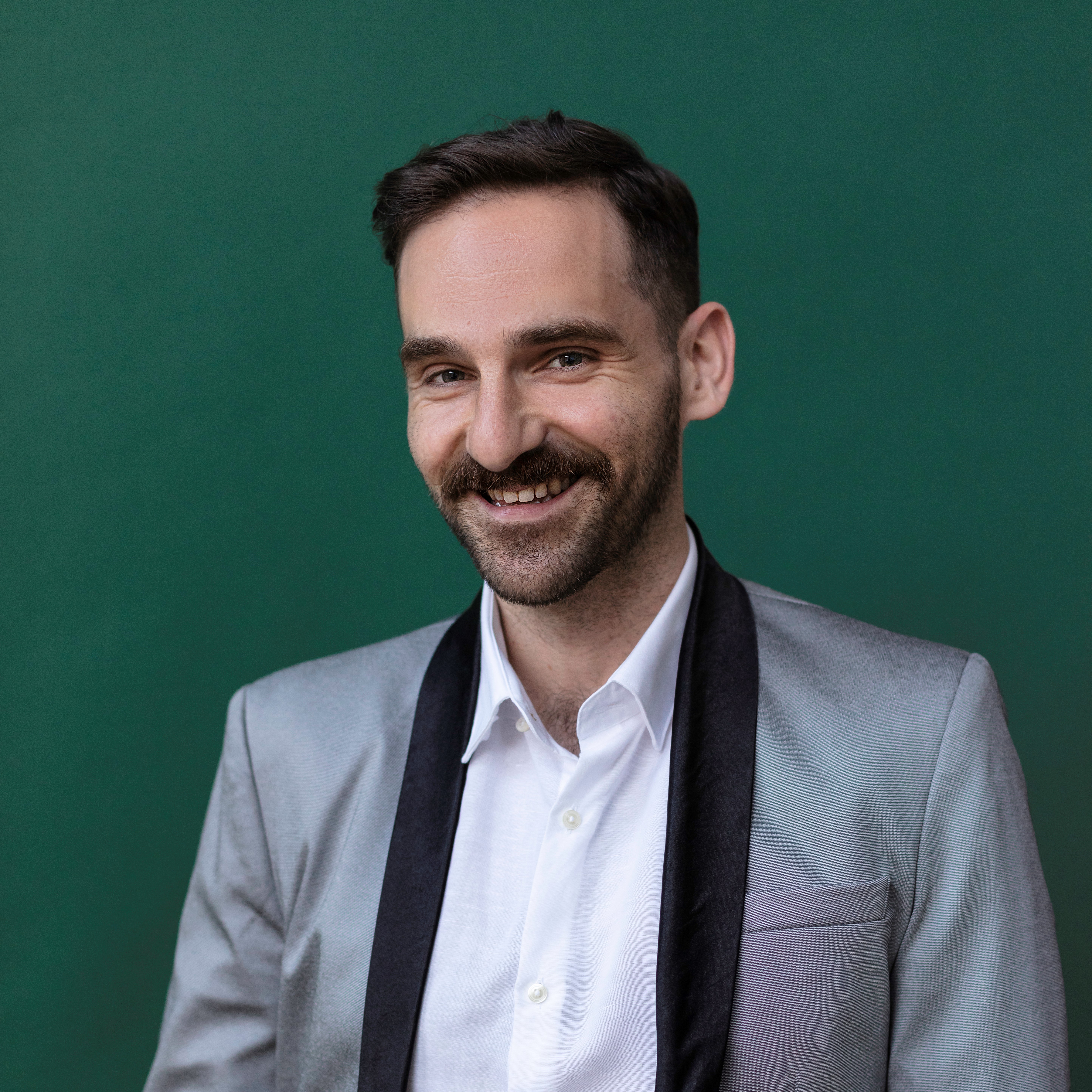 Giacomo Nudi looking directly at camera and smiling. He is wearing a white, collared shirt and a light grey vest with black lining.