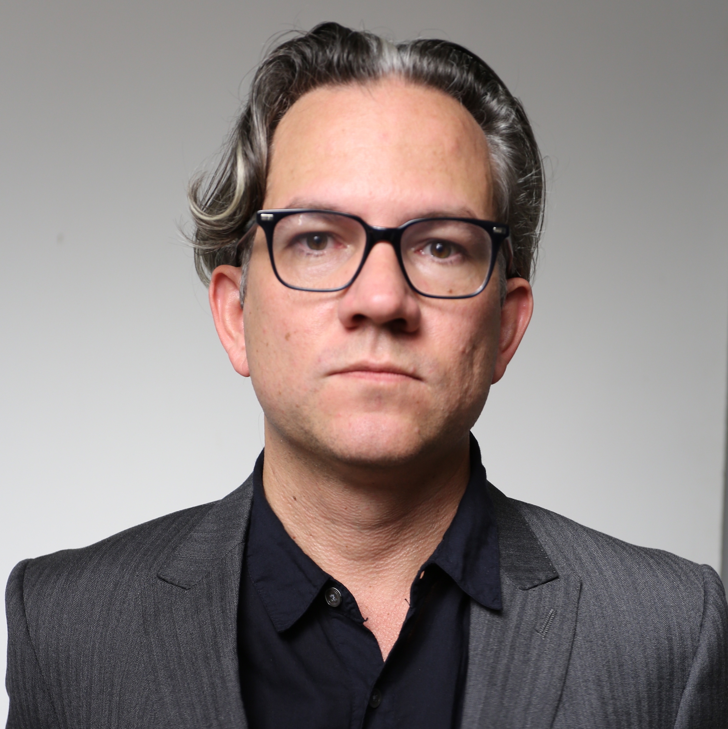 Hugo Perez, a white man wearing a suit and glasses, looks directly at the camera.