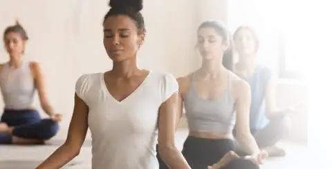 Group of women of different ethnicities sitting in a restful cross legged yoga posed, eyes closed in a mindful meditation.