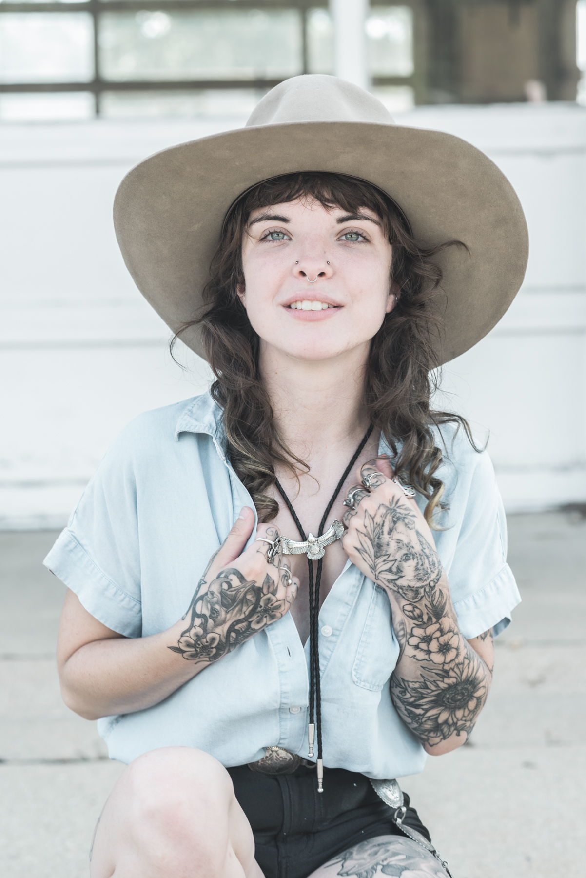 portrait of Maddie in a blue shirt and black shorts wearing a large hat and a bolo tie.