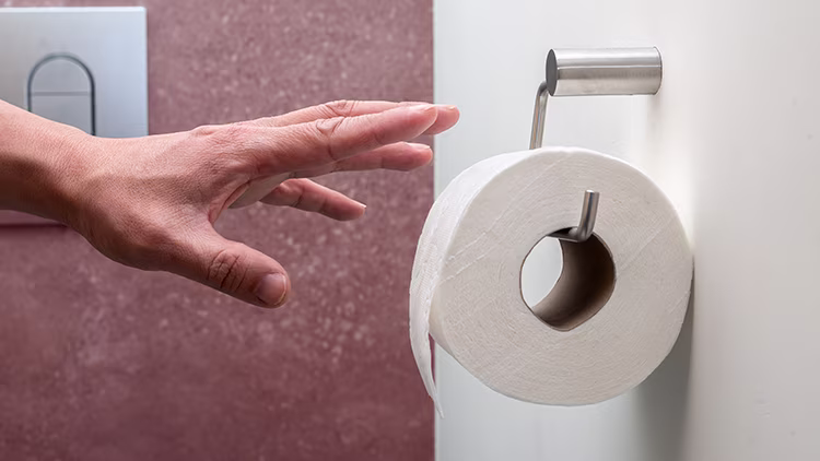 A hand reaching out to tissue roll in bathroom.