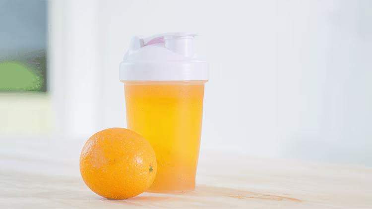 Orange juice in a bottle and an orange placed next to with white background.