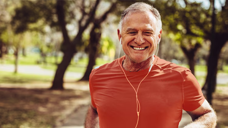 A man smiling in orange t-shirt running in park with earphone.