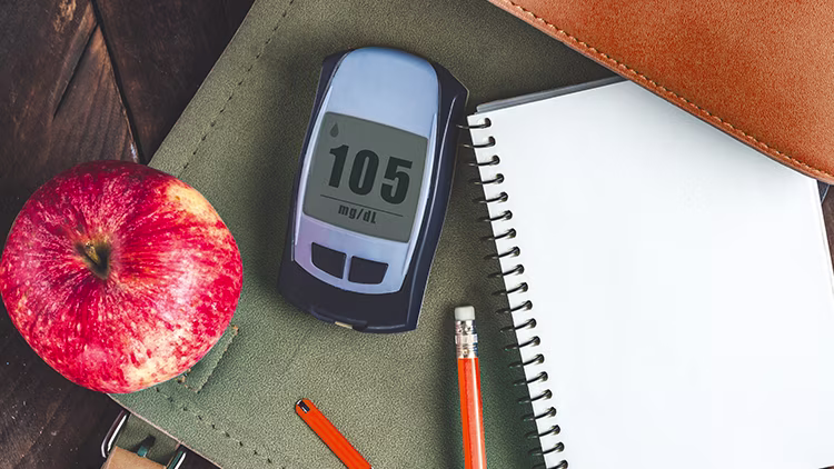 Glucometer reading 105 placed on the table along with an apple, pencil and note.
