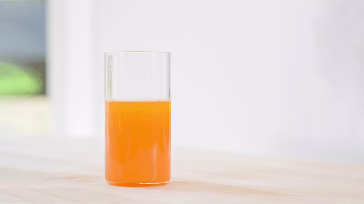 A glass of orange juice placed on a table with white background.