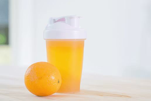 Orange juice in a bottle and an orange placed next to with white background.