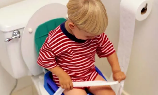 Boy holding toilet paper while sitting on bathroom toilet