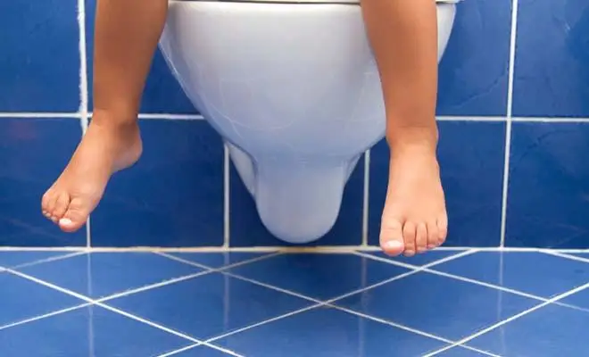 Deux petits pieds se balancent, tandis qu'on devine un enfant assis sur la toilette.