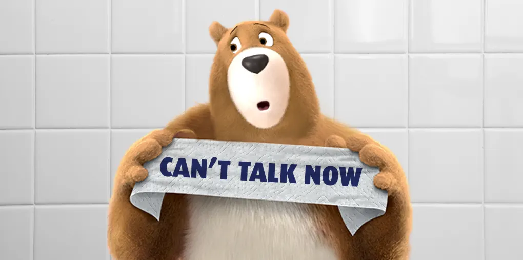 L'ours Léonard tient une banderole de papier hygiénique sur laquelle est écrit le message « Can't Talk Now » signifiant Je ne peux pas parler en ce moment.
