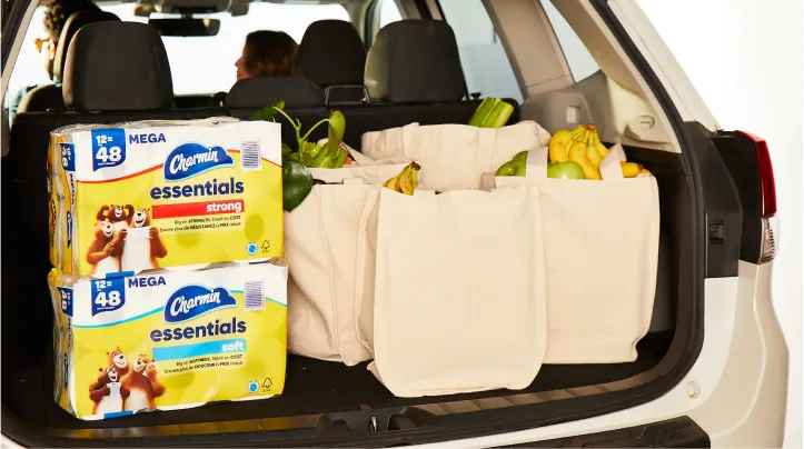 On voit des emballages Charmin Essentials Strong et Soft dans le coffre d'une voiture, avec les sacs d'épicerie.