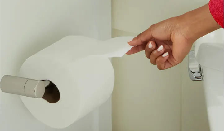 Une main de femme tire une feuille d'un rouleau de papier hygiénique installé sur un porte-rouleau.