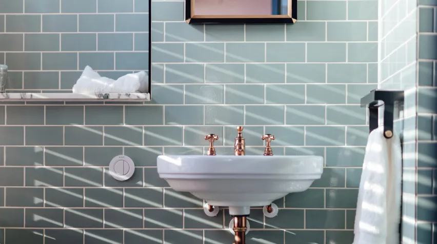 Salle de bain aux carreaux gris-vert sur lesquels une lumière douce crée les motifs.