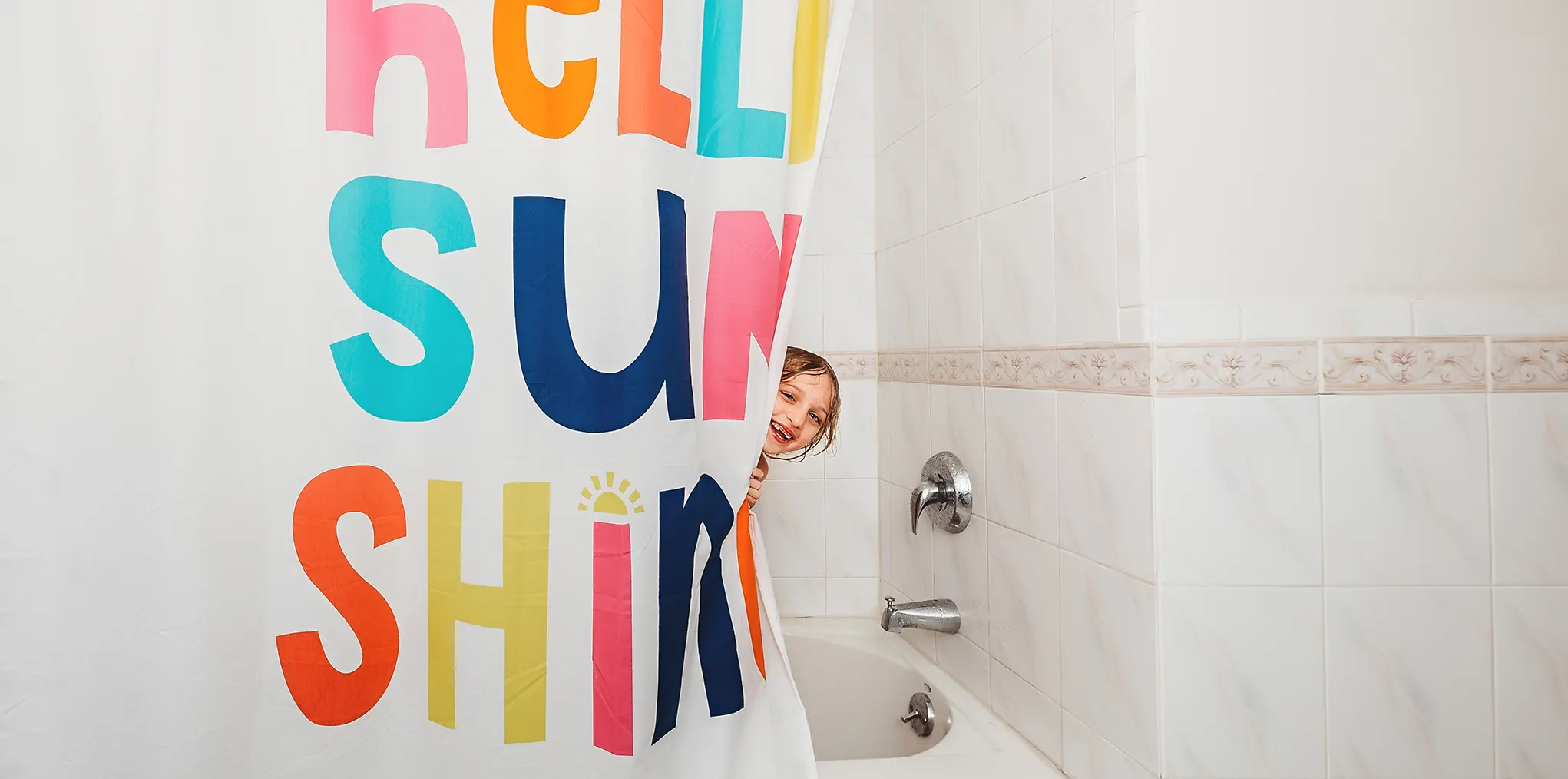 Une fillette se penche la tête hors d'un rideau de douche où sont écrits les mots « Hello Sunshine » signifiant Bonjour rayon de soleil.