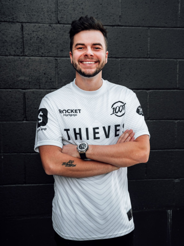 Nadeshot smiling with arms crossed in front of black brick wall