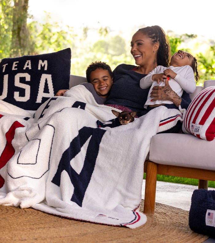 A woman with her son, daughter, and dog wrapped in the CozyChic Team USA Multi Color Throw with the CozyChic Team USA and Stars and Stripes pillow.  